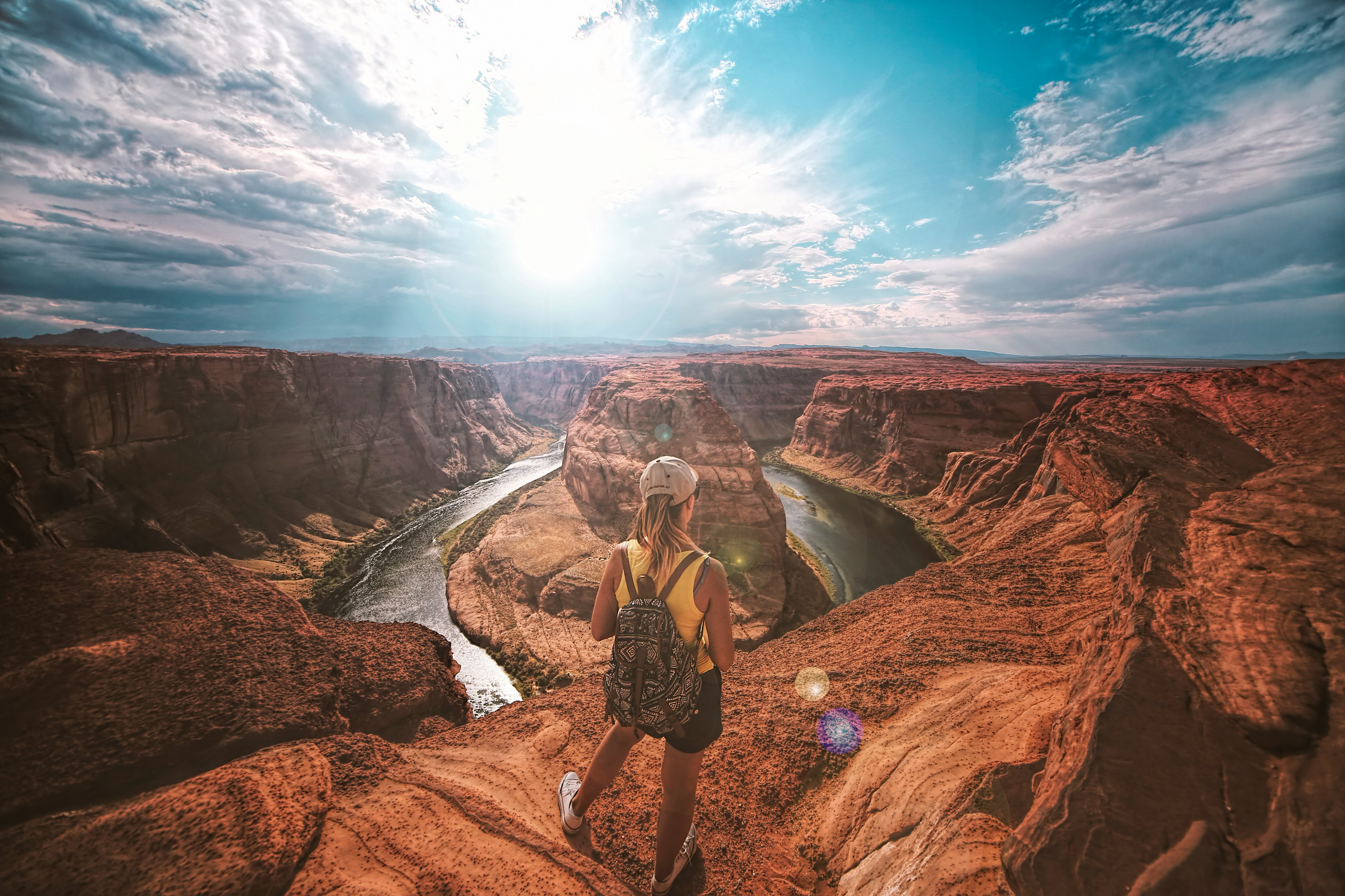 Eine junge Frau steht mit Rucksack und Cap vor einem Canyon.