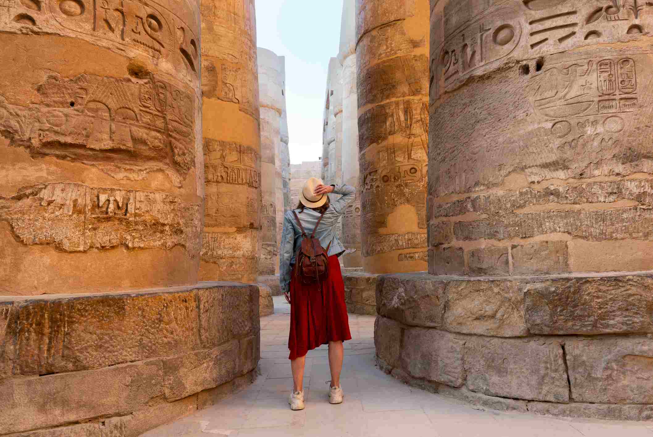 eine-frau-im-roten-kleid-steht-zwischen-historischen-ägyptischen-säulen