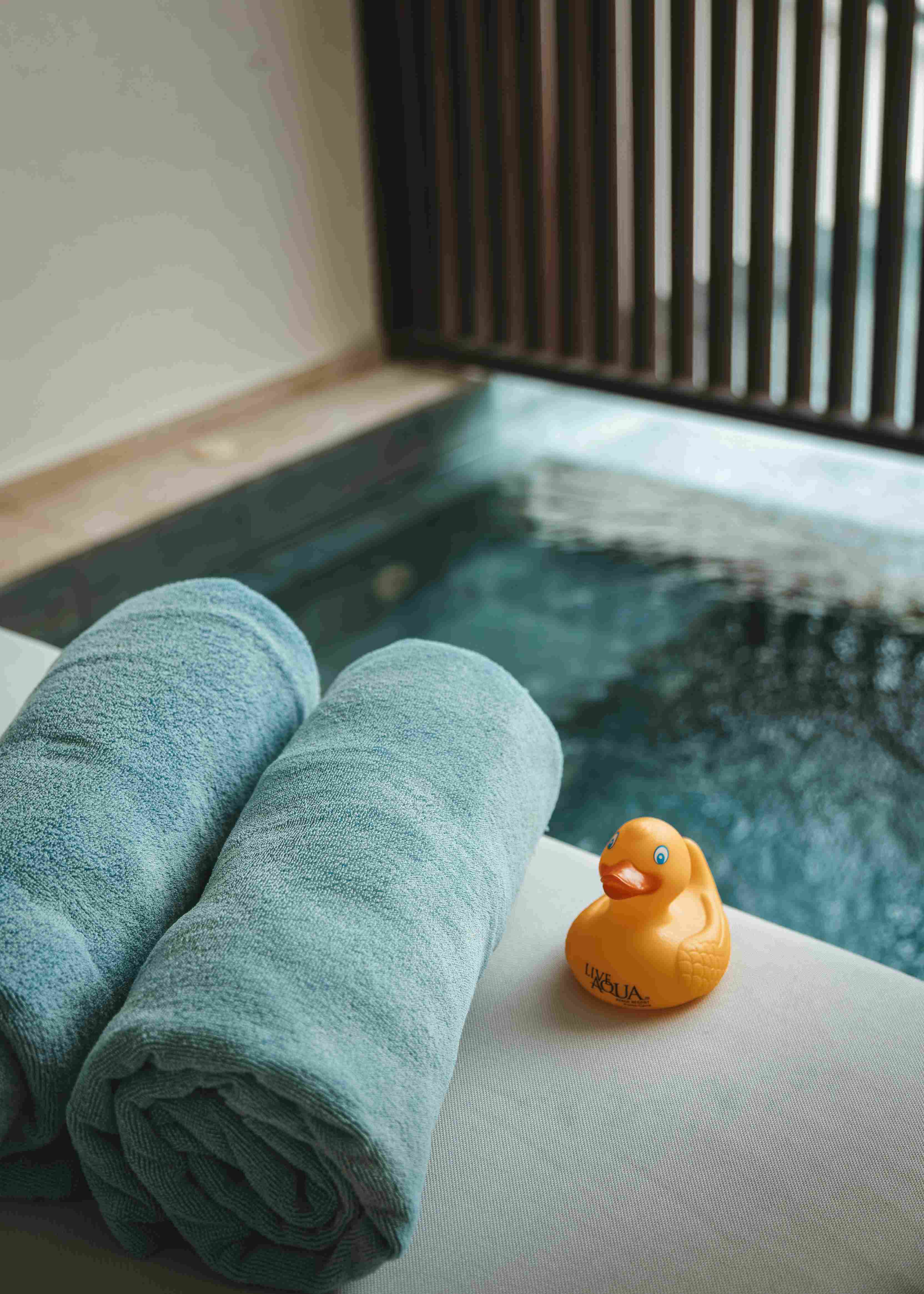 Zwei graue Handtücher und eine gelbe Quitscheente liegen am Rand eines Pools im Wellnessbereich