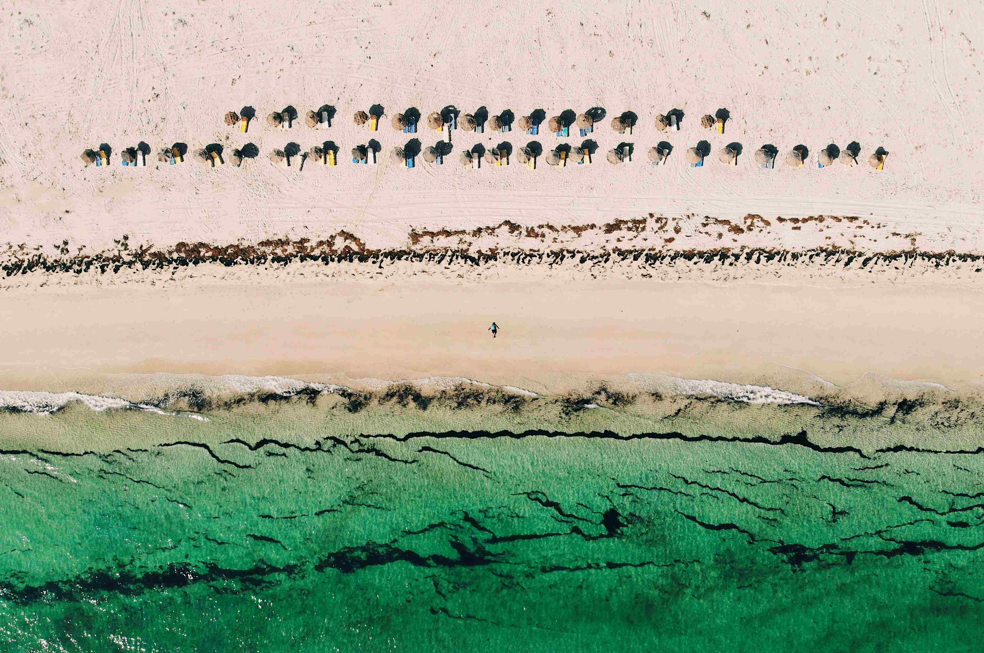 Eine Luftaufnahme eines leeren Sandstrands mit Sonneschirmen und grünem Wasser