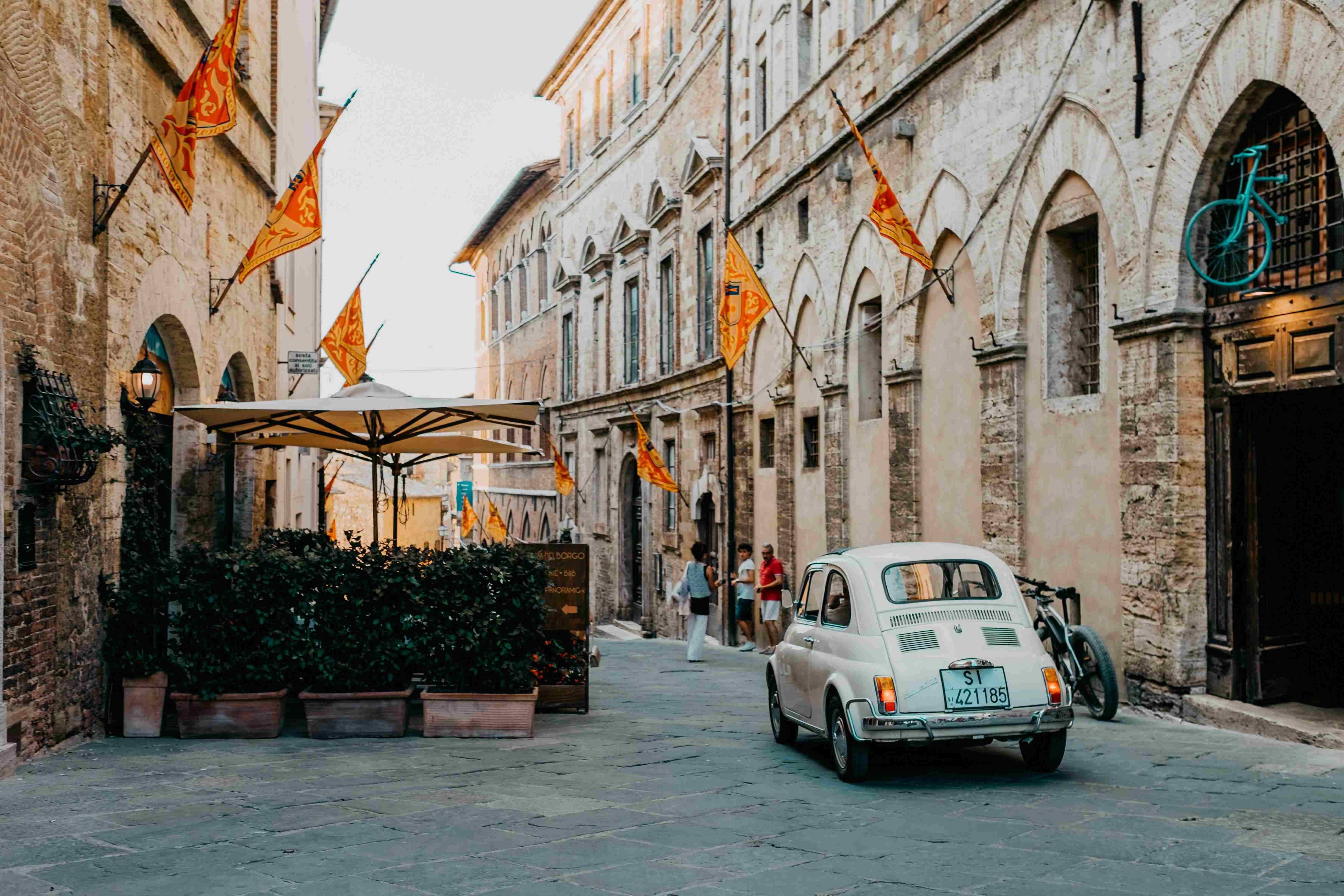 In einer historischen Straße mit gelb-roten Flaggen steht ein alter Fiat