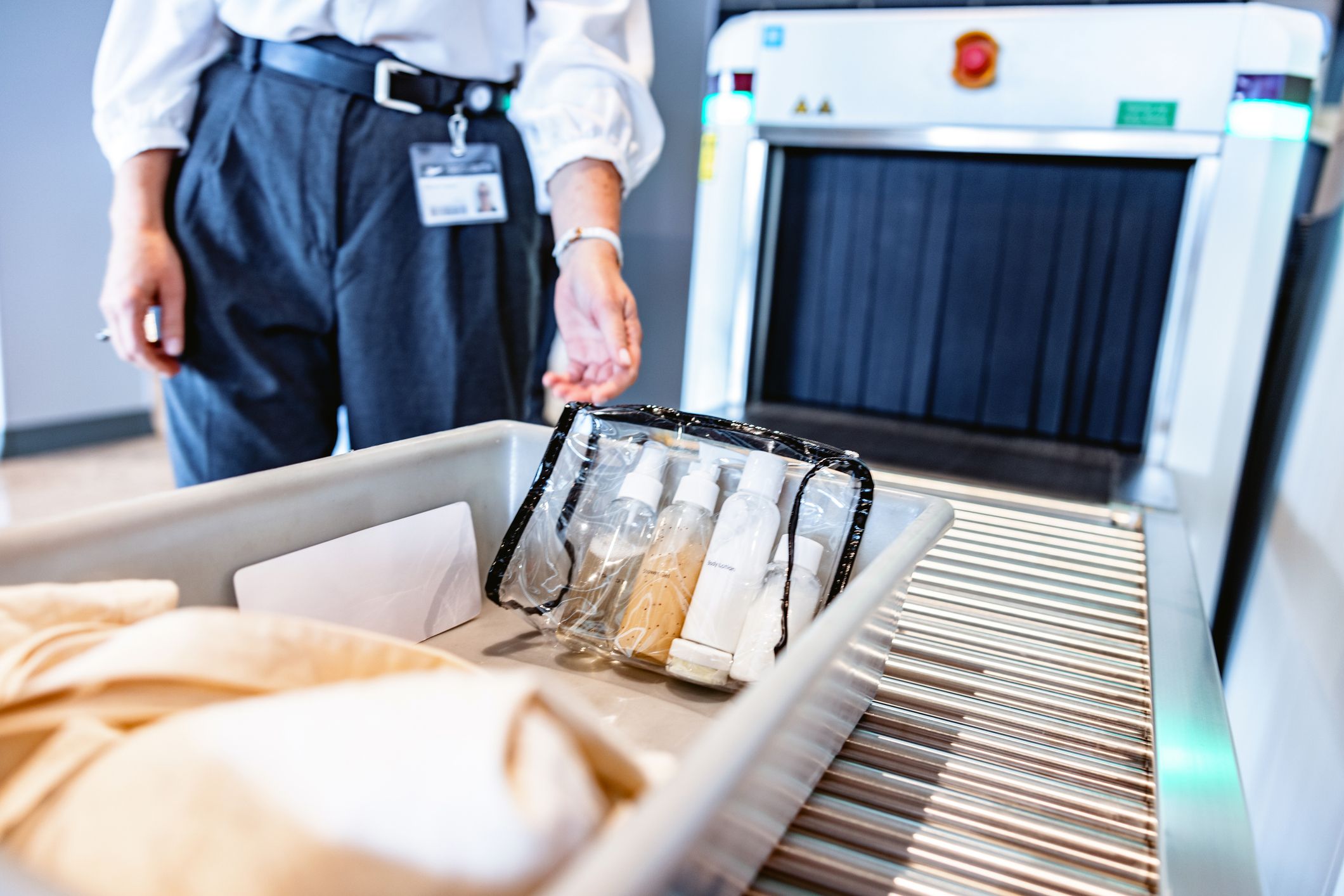 Eine Box mit Gepäckinhalten und einem durchsichtigen Plastikbeutel mit Flüssigkeiten kurz vor dem CT-Scanner einer Sicherheitskontrolle am Flughafen