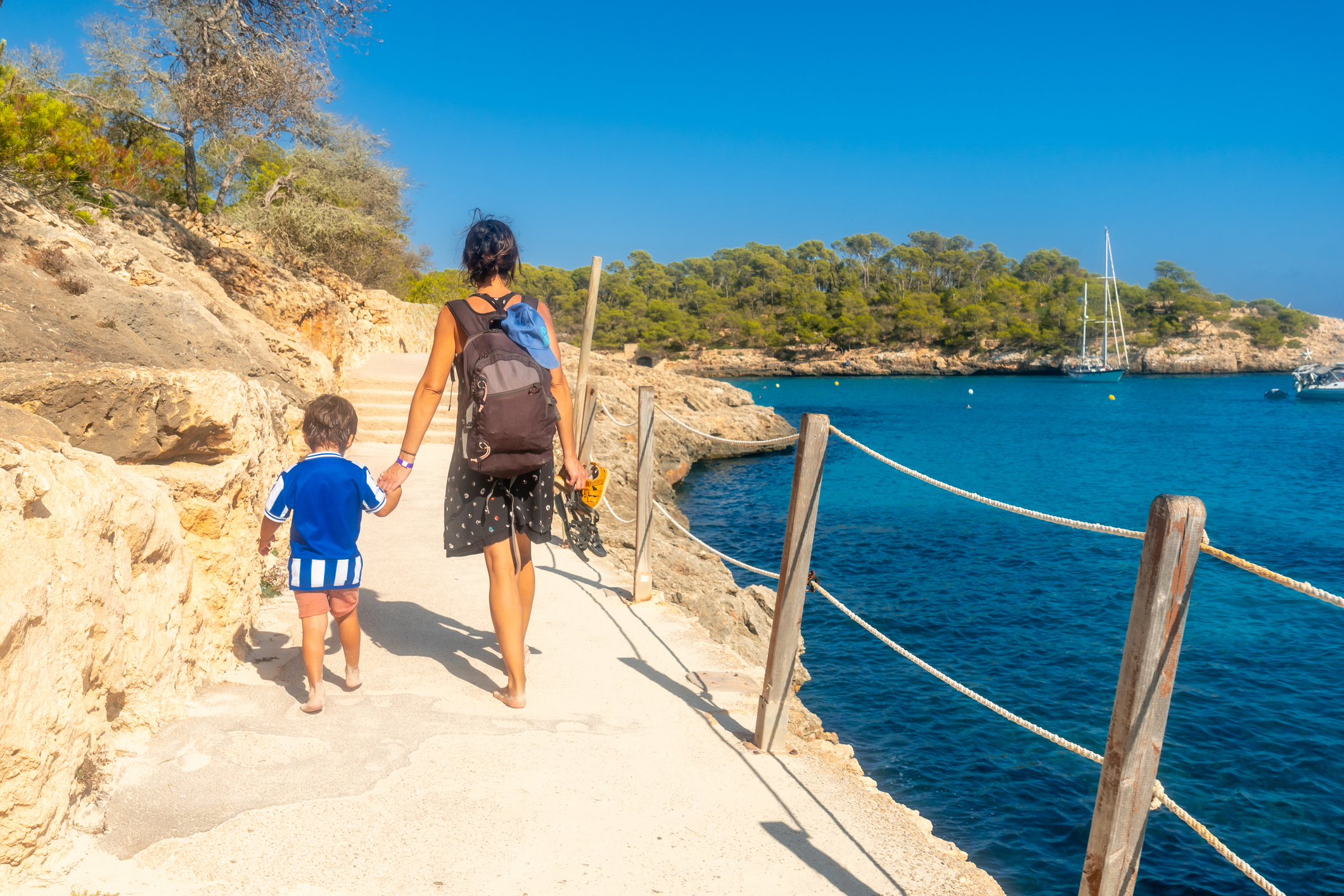 Mallorca Strände: Eine Mutter mit Kind in der Hand läuft einen Strandweg entlang