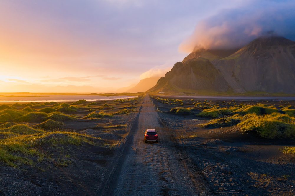 Ein Auto fährt durch eine einsame, grüne Landschaft im Hintergrund Vulkane