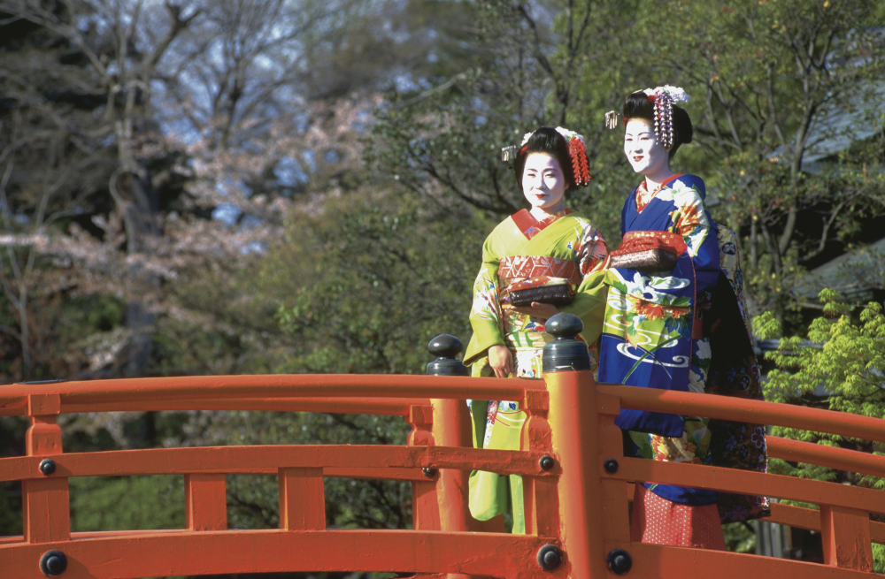 Auf einer Holzbrücke stehen zweo japanische Frauen in traditioneller Kleodung