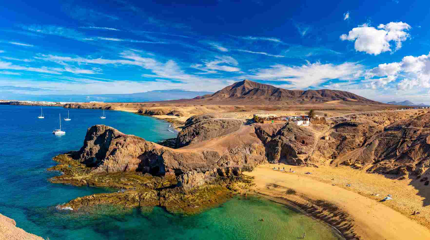 lanzarote-urlaub Eine trockene, vulkanartige Lanschaft direkt an der blauen Küste mit weißen Segelboten