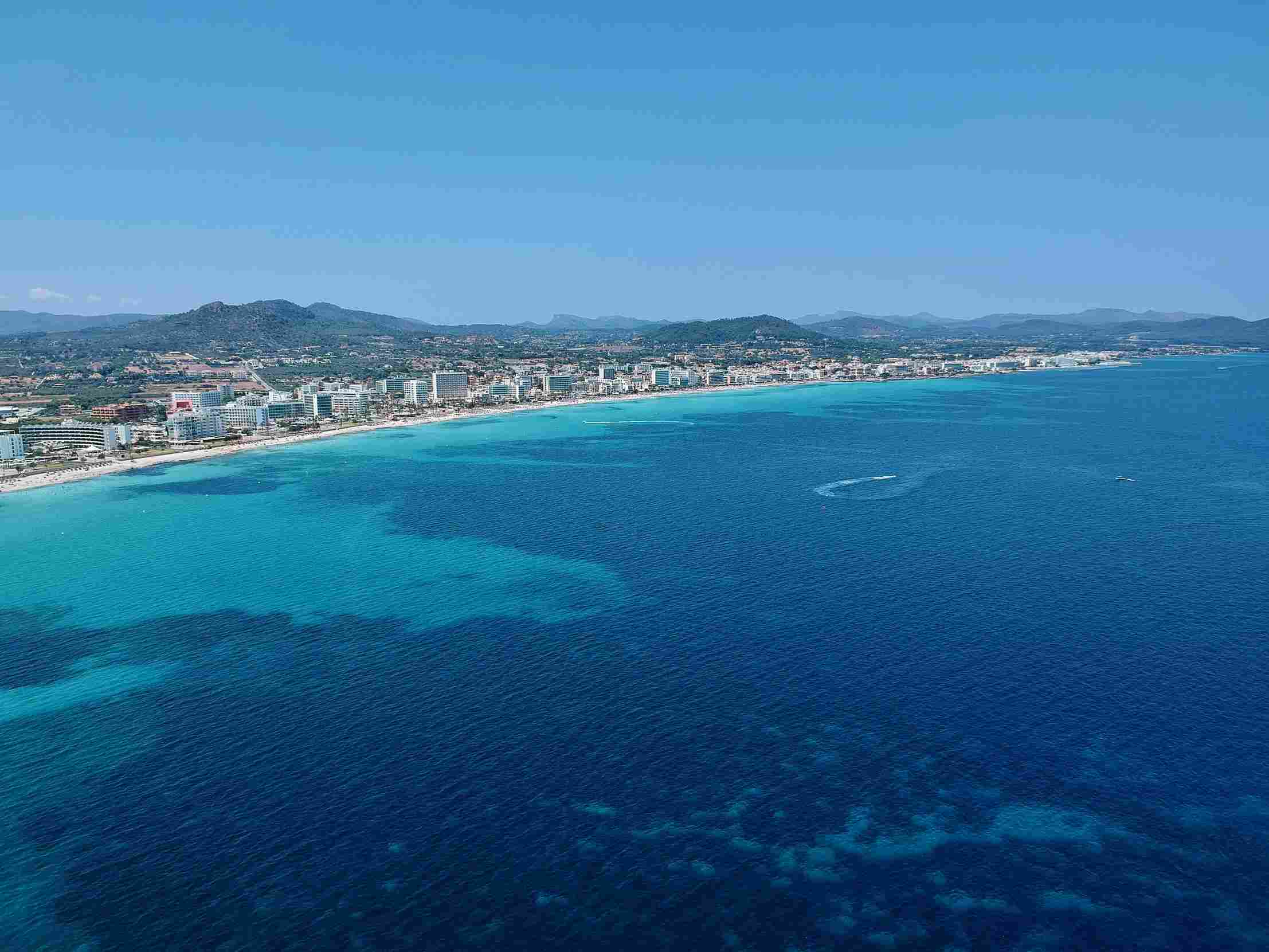 top10-günstige-reiseziele-mallorca das-tief-blaue-türkise-meer-grenzt-an-einen-sehr-langen-sandstrand-mit-einer-stadt