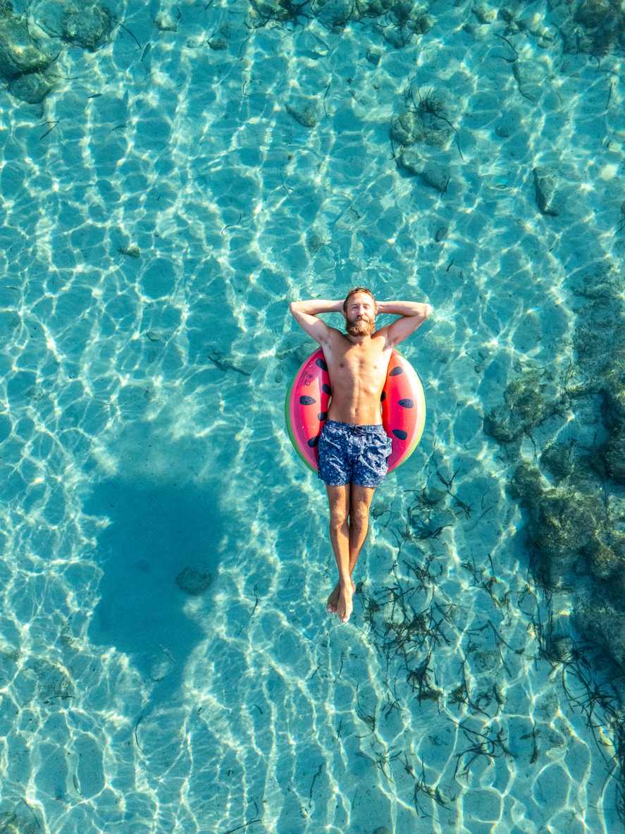 Ein Mann liegt entspannt auf dem Rücken auf einer Luftmatratze im türkisen Wasser