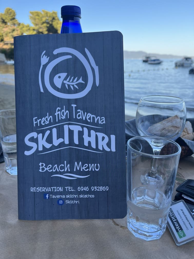 Skiathos Taverne Ein gedeckter Tisch mit Gläsern und einer Speisekarte einer Taverne mit Fischangebot
