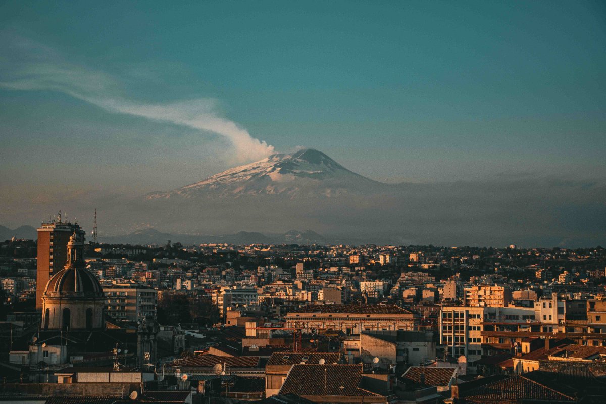 Eine italienische Stadt im Hintergrund der mit Schnee bedeckte, rauchende Ätna-Vulkan