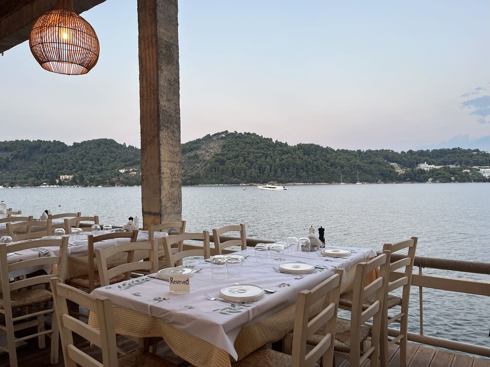 skiathos-hafenrestaurant Ein Tisch mit weißer Tischdecke und Stühlen in einem überdachten Restaurant am Meer