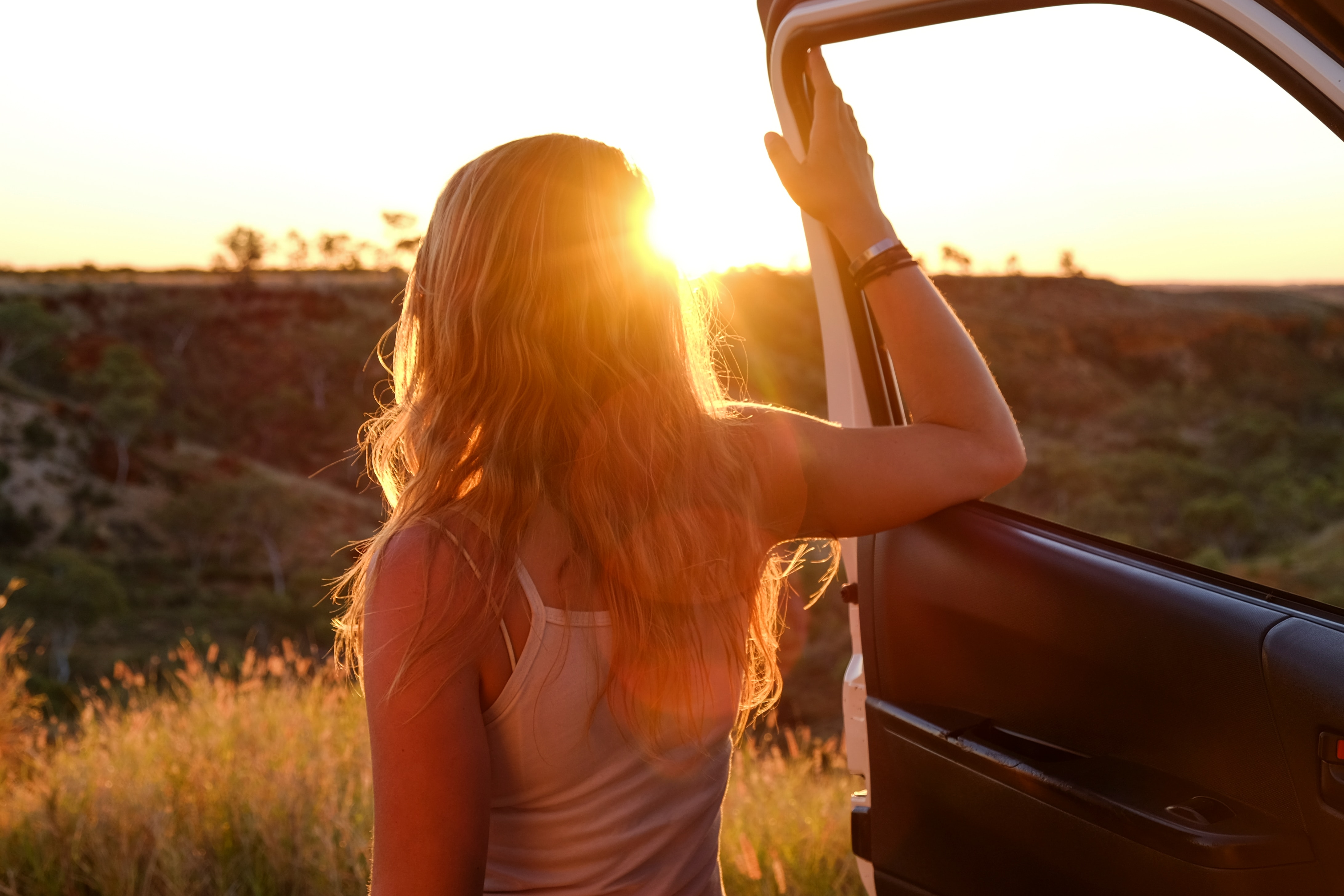 mietwagen-urlaub Eine junge Frau öffnen die Autotür und blickt in den Sonnenuntergang