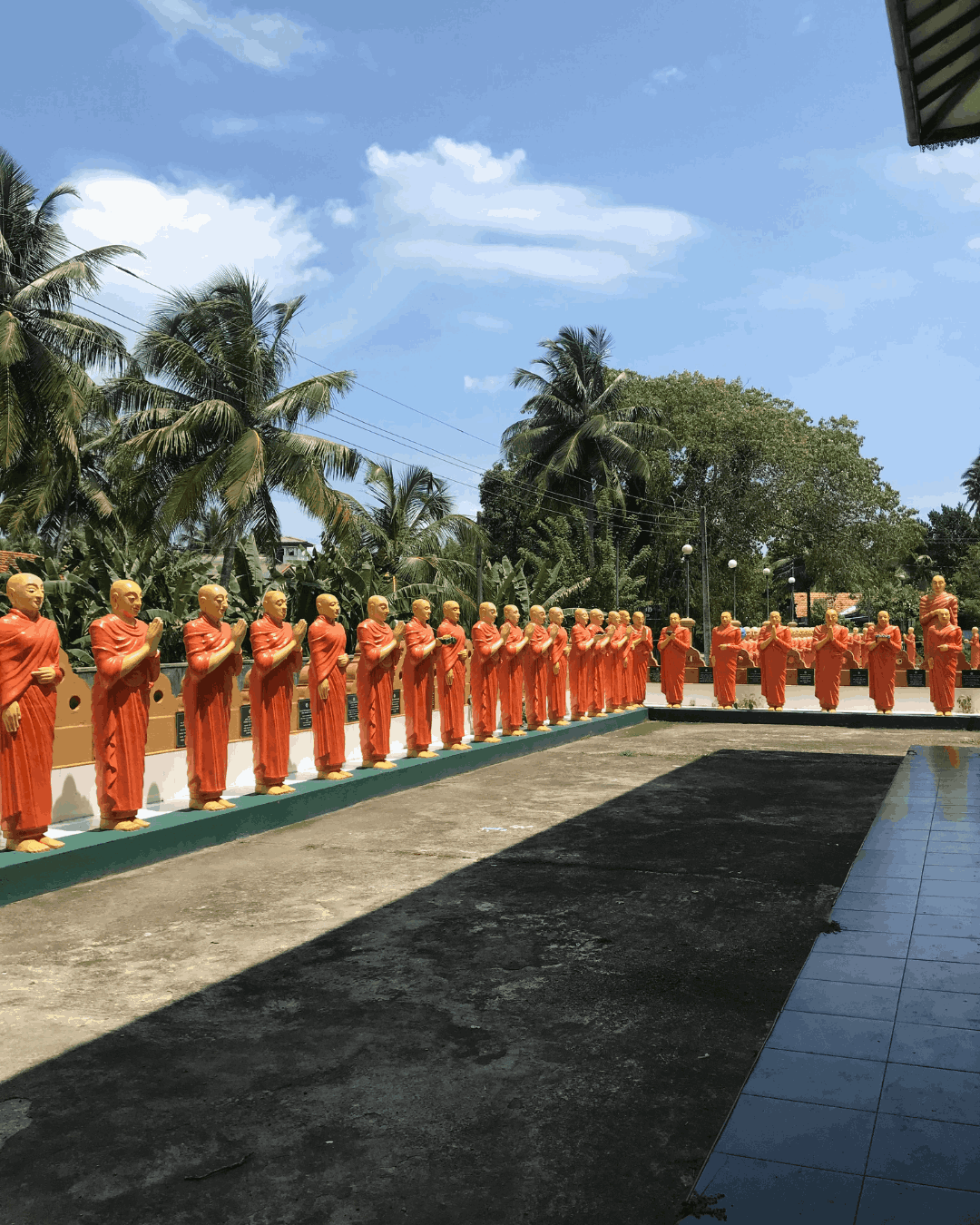 sri-lanka-buddhistische-statuen Um einen Tempel vor Palmen stehen unzählige Mönchsstatuen in orangenen Roben.
