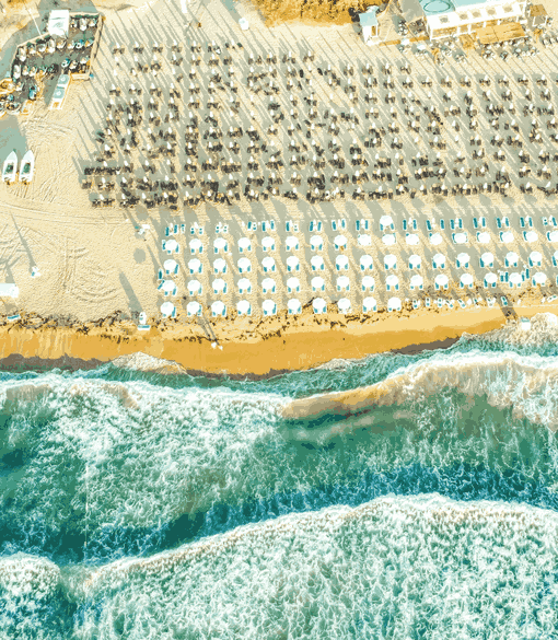 Eine Luftaufnahme eines lebhaften Strands mit vielen Sonnenliegen und -schirmen