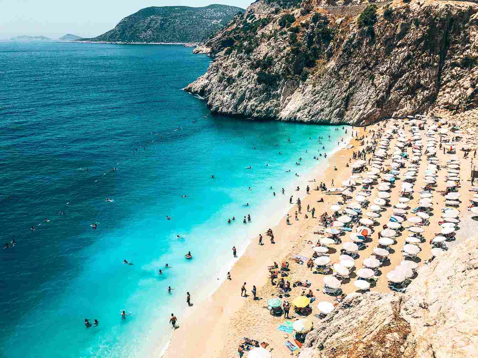 top10-günstige-reiseziele-türkei ein-belebter-strand-mit-sonnenliegen-undschirmen-zwischen-felsen