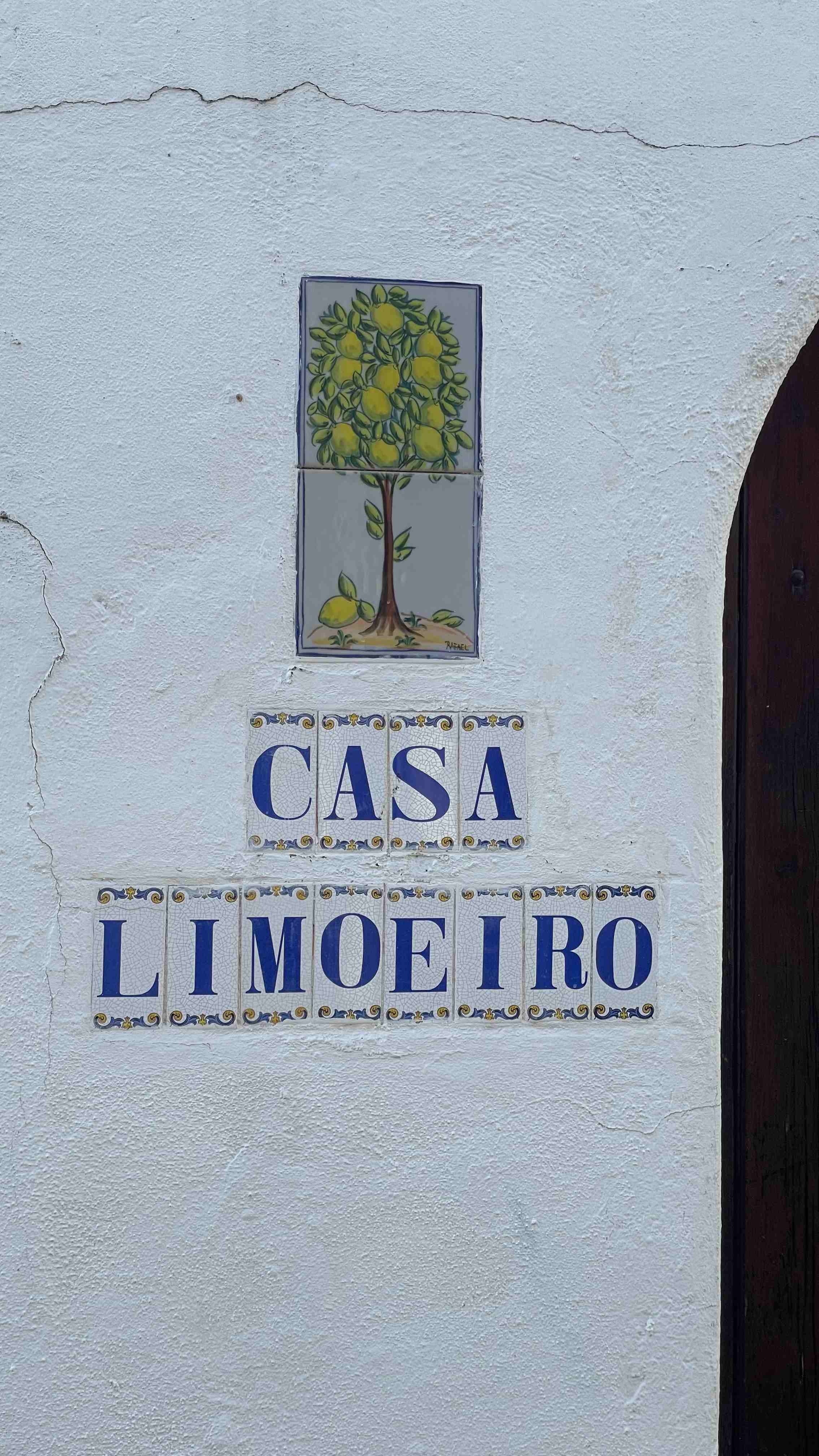 algarve-hausfassade-mit-schild An einer weißen Hausfassade steht ein Schild mit einem Zitronenbaum und der Aufschrift "Casa limoeiro"