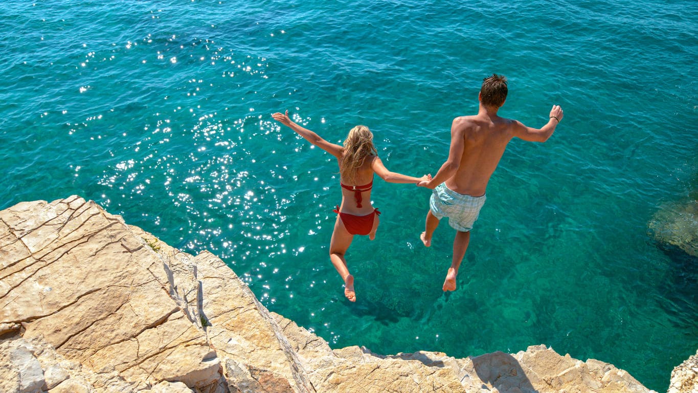 Pärchen springt von einem Felsen ins Meer