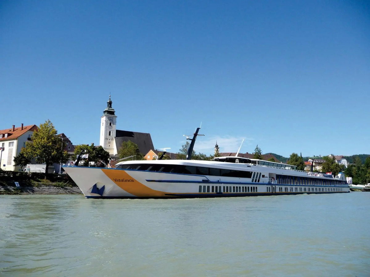 flusskreuzfahrt-1avista-silvester Ein weiß-gelbes Flusskreuzfahrtschiff gleitet auf einem ruhigen Fluss