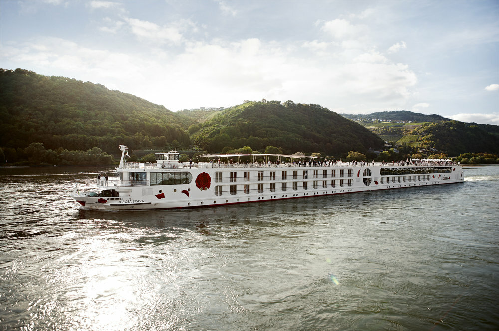 Ein weißes Flusskreuzfahrtschiff mit roten Blüten der Reederei A-ROSA gleitet auf einem Fluss entlang