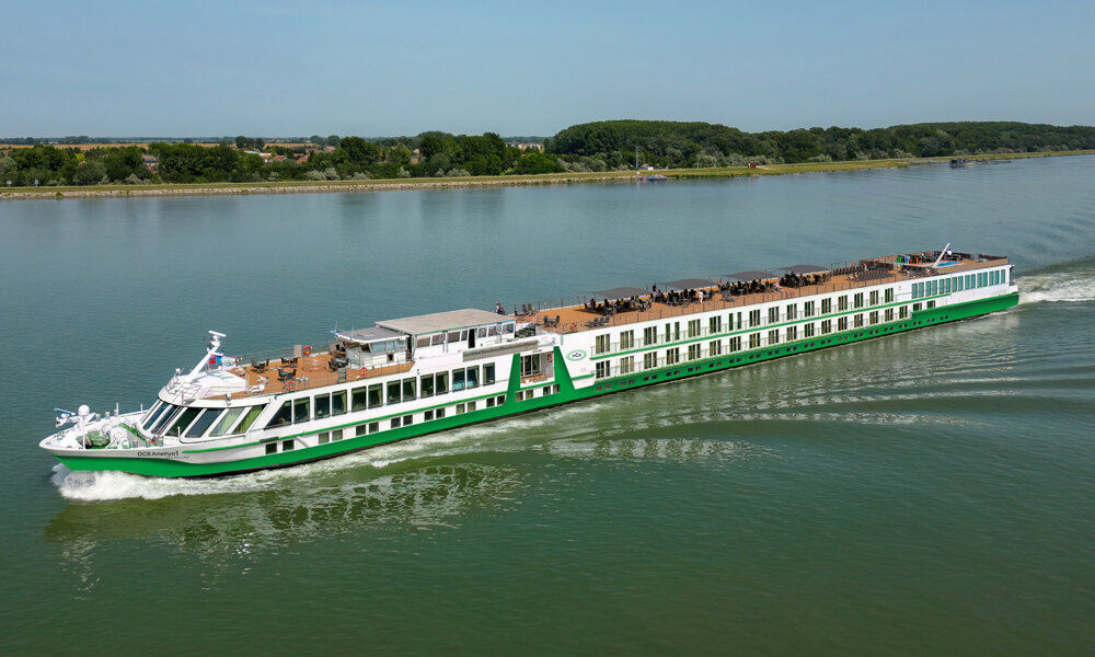 flusskreuzfahrten-europa-dcs-donau Ein grün-weißes Flusskreuzfahrtschiff der Reederei DCS gleitet auf der grünlichen Donau
