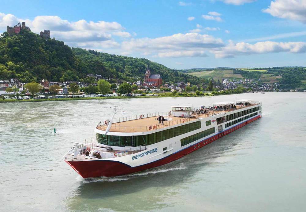flusskreuzfahrten-europa-nicko-cruises-rhein Ein weiß-rotes Flusskreuzfahrtschiff der Reederei nicko Cruisees gleitet auf einem Fluss durch eine grüne Landschaft
