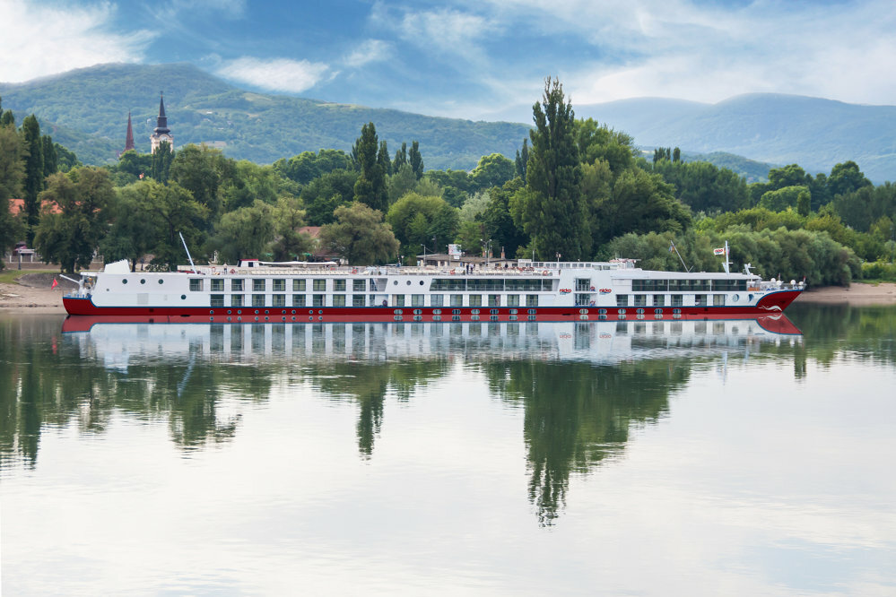 lusskreuzfahrten-europa-nicko-donau Ein Flusskreuzfahrtschiff der Reederei nicko Cruises liegt an einem Hafen an einer grünen Landschaft an