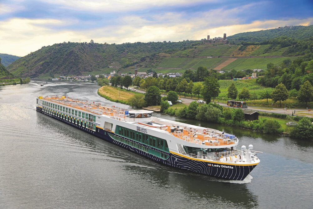 Ein Flusskreuzfahrtschiff der Reederei "plantours" gleitet auf dem Rhein durch eine grüne Landschaft