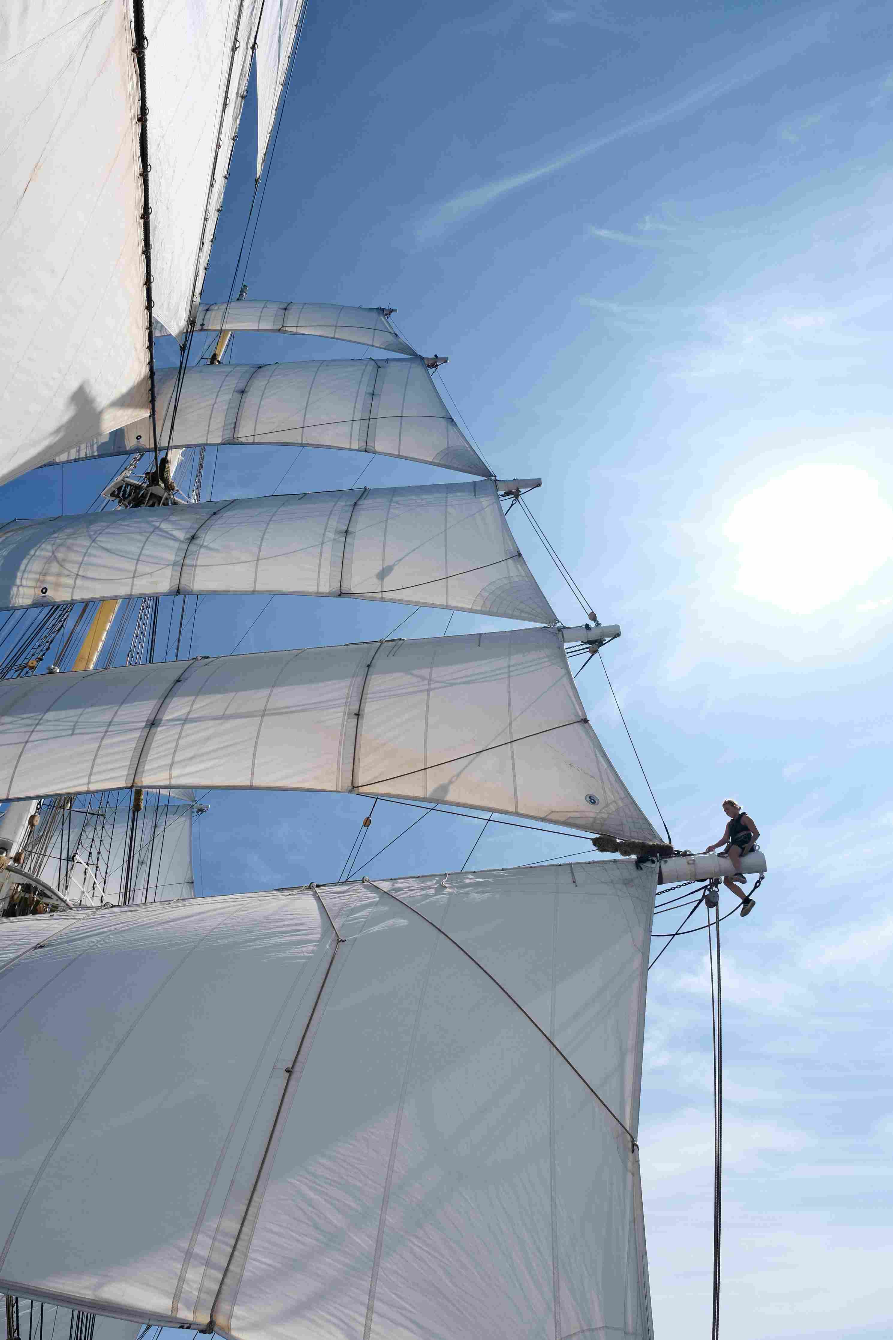 segelkreuzfahrten Eine Frau sitzt auf dem Segelträgers eines Segelschiffs