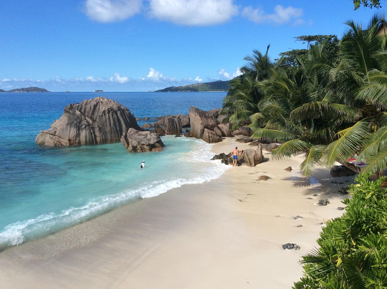Goldgelber Strand mit Palmen und einem Hotel im Hintergrund sowie Felsen Goldgelber Strand mit Palmen und einem Hotel im Hintergrund sowie Felsen