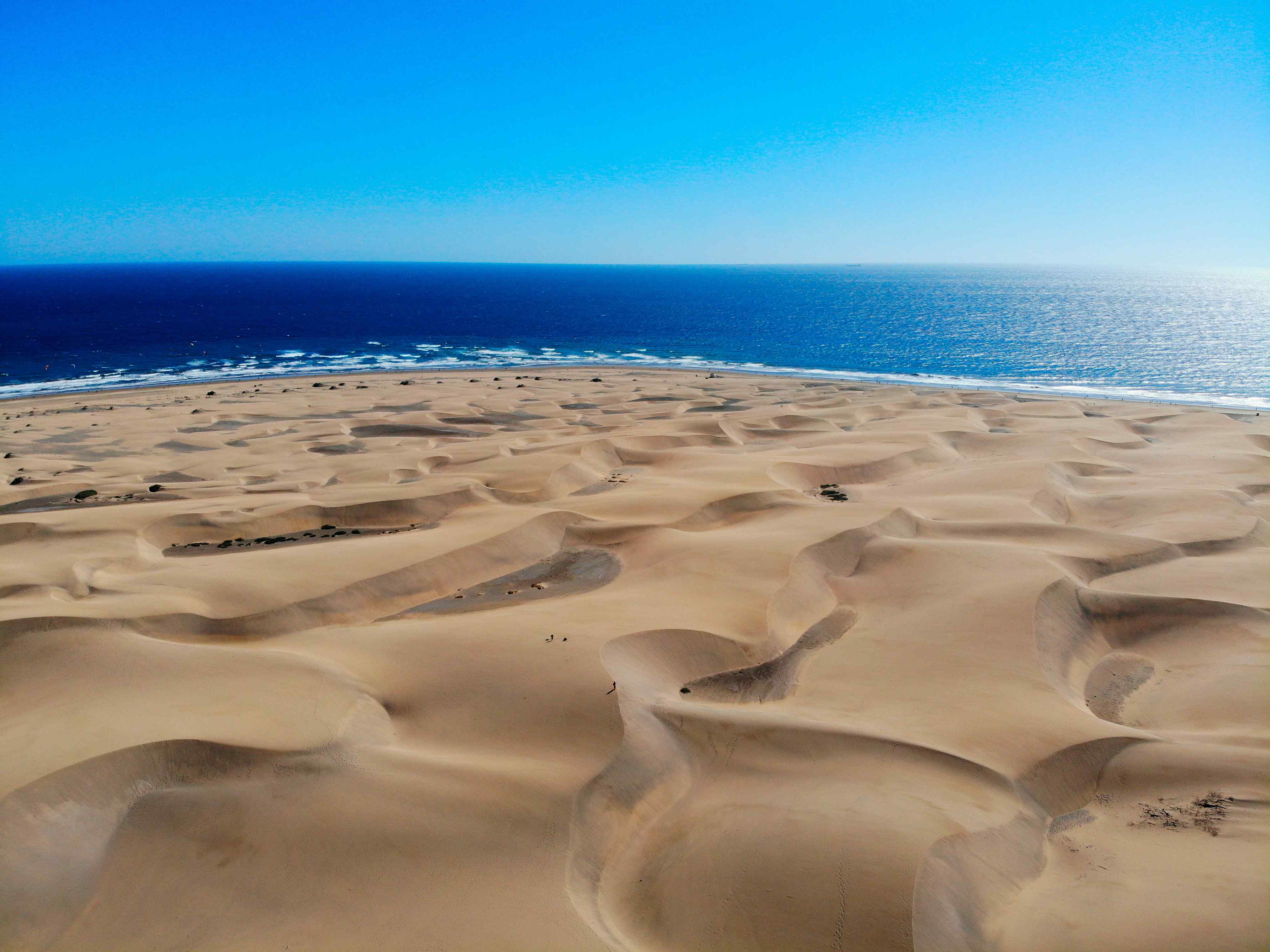 grand-canaria-urlaub Ein Wüstenlandschaft direkt am tiefblauen Meer unter blauem Himmel.