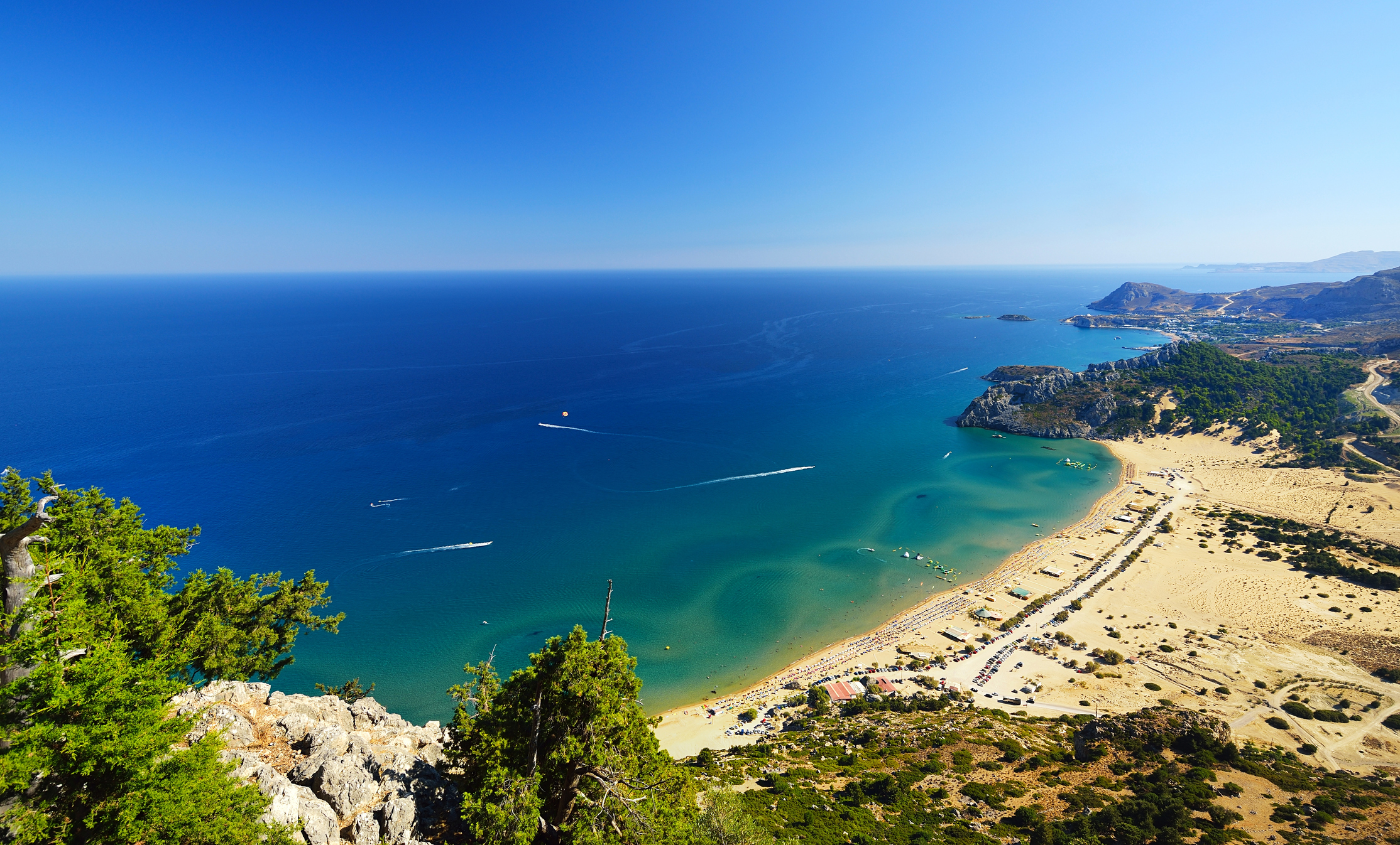Türkisblaue Bucht mit hellem feinsandigen Strand und Strandliegen und grüner Umgebung
