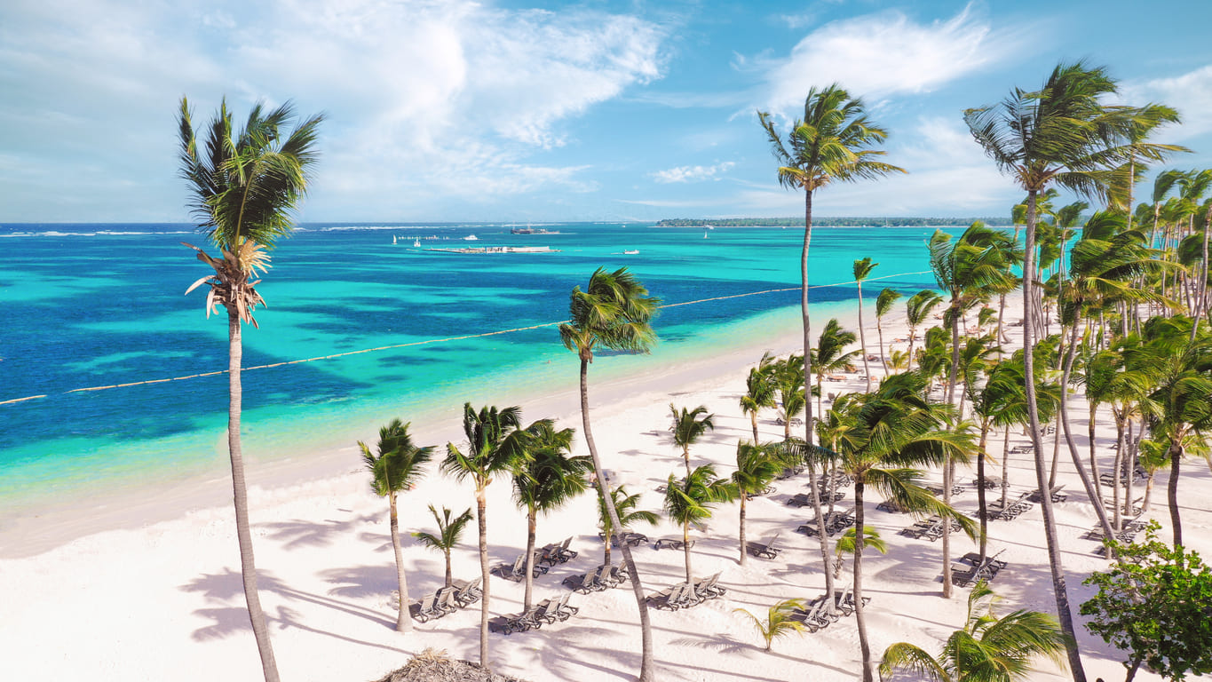 Blick von oben auf einen weißen Strand mit Palmen und wenigen Menschen Blick von oben auf einen weißen Strand mit Palmen und wenigen Menschen