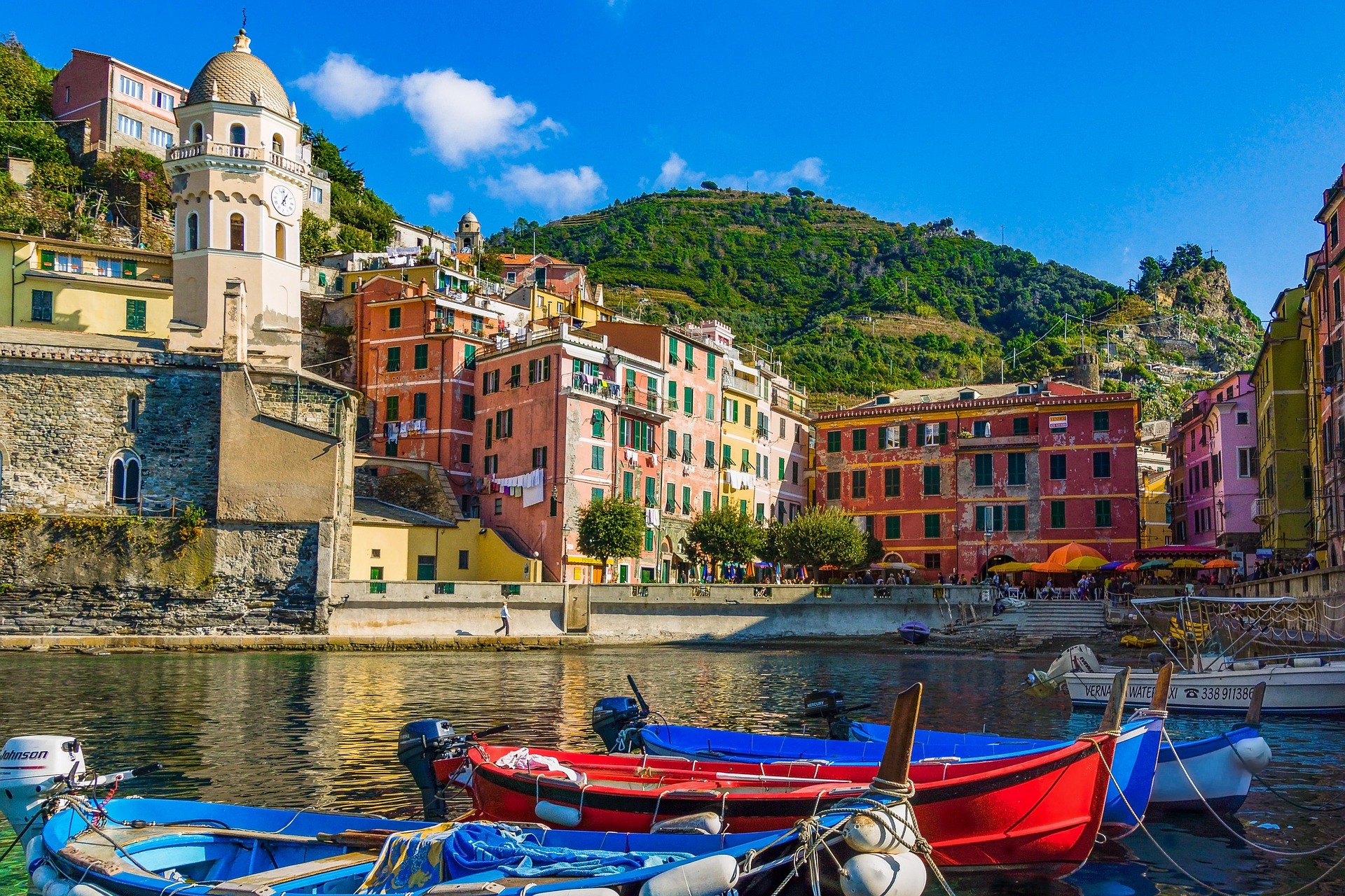 Italien Urlaub Kleiner städtischer Bootshafen mit Booten und Häusern sowie grünen Hügeln