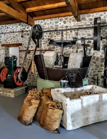 olivenölproduktion-maschinen Eine historische Maschine zur Olivenölproduktion und diversen Säcken voller Oliven