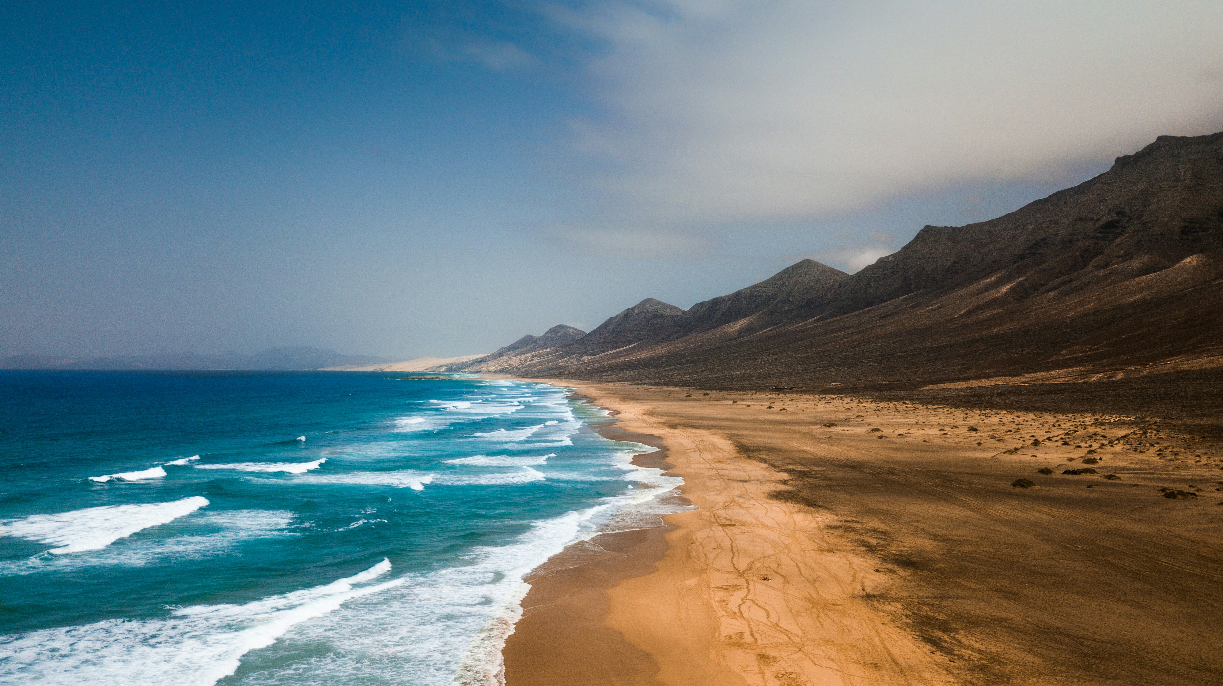 Ein langer, breiter Sandstrand mit Dünen und Sandlandschaft am blauen Meer.