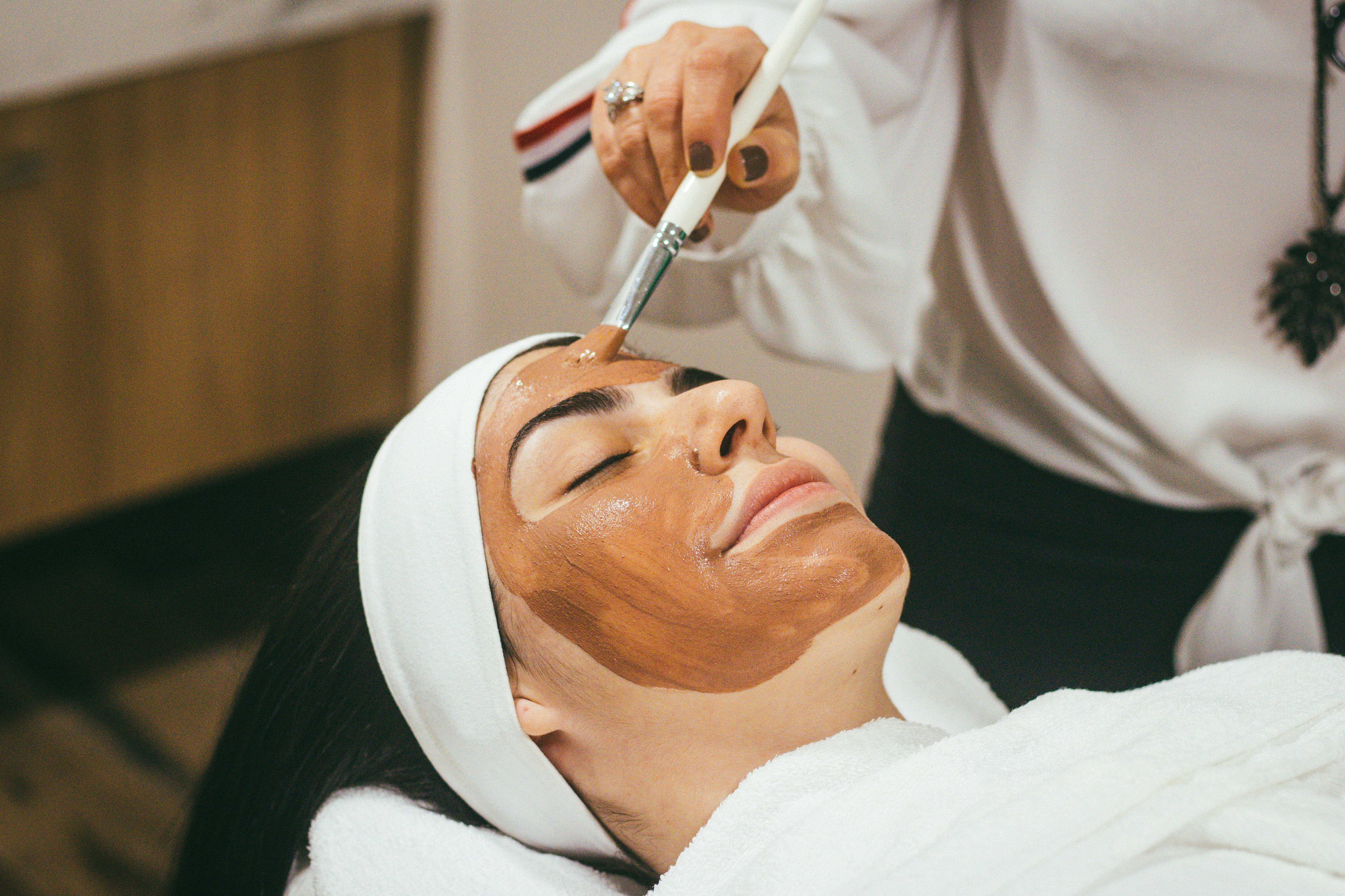 Beauty-Maske Eine Frau liegt entspannt im Bademantel und Haarband und bekommt eine Gesichtsmaske aufgetragen.