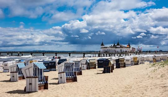 Strandkörbe stehen am hellen Ostseestrand mit leichtbewölktem Himmel