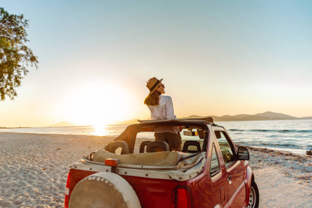 Eine Frau steht in einem Jeep im Abendlicht mit untergehender Sonne